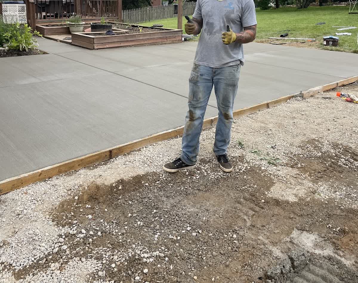 A freshly poured and floated concrete patio slab behind a house, edges formed and the surface still wet.